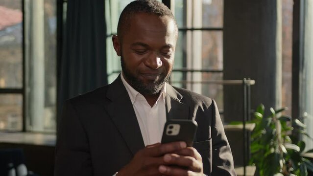 Mature 40s African American ethnic man businessman in office thinking typing message email on mobile phone cellphone has doubt unsure think ponder business idea happy worker come up with good decision