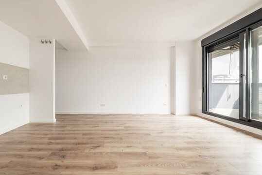 Living room of an empty apartment with light wooden floors and access to a terrace