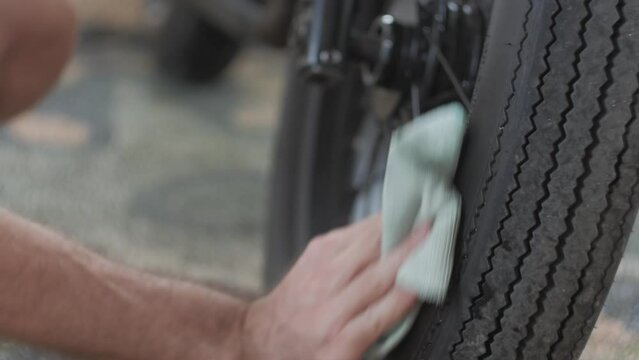 Man polishes classic motorcycle tire with shiny tire kit and napkin. The tilt shot follows the bike maintenance activity before the rider does before a cafe racer event. Detail shot of wheel cleaning.