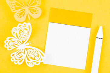 The blank paper note for reminder and carve of paper butterfly with the pen on yellow background, space for text.