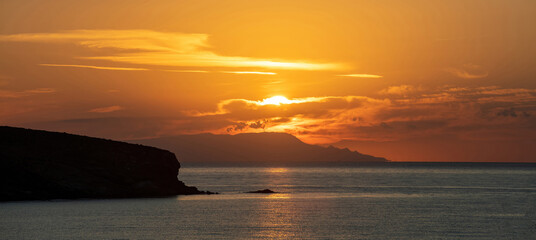 Sunset over Greek island, Cyclades, Greece. Golden sun hides behind cloud. Sparkle sea. Banner
