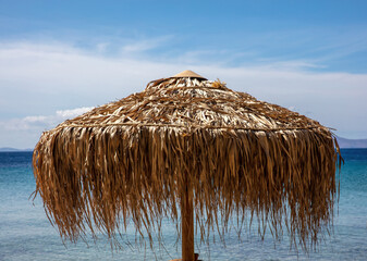 Straw umbrella at beach close up view. Sunny day Aegean sea water blue sky. Greece Cyclades island.