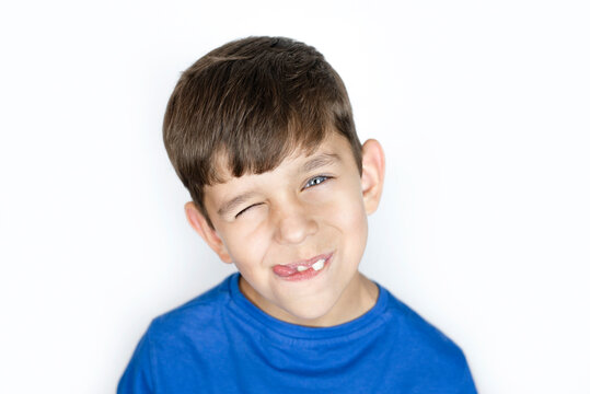 A young boy, still almost a child, with sly, satisfied face, smiles, squinted at one eye and shows his tongue, portrait of a young boy with a sly face on a white background