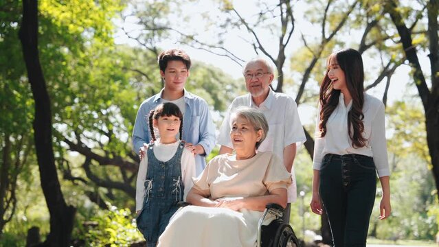 Asian Big family walking together and senior woman sitting on wheelchair in the park on long weekend
