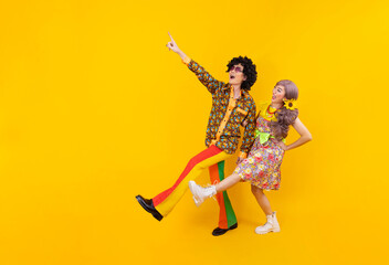 Fototapeta na wymiar Asian hippie couple dress in 80s vintage fashion with colorful retro clothing while dancing together isolated on yellow background for fancy outfit party and pop culture concept