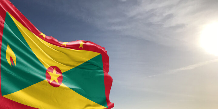 Grenada national flag cloth fabric waving on beautiful grey sky Background.
