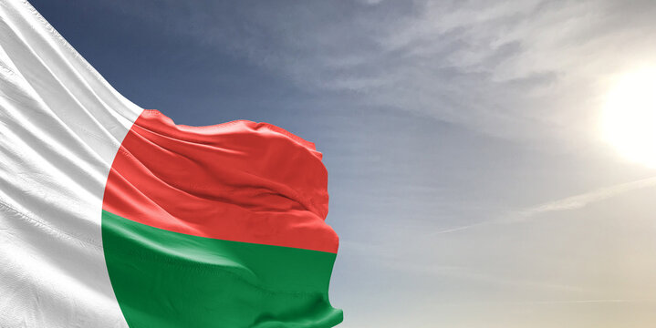 Madagascar national flag cloth fabric waving on beautiful grey sky Background.