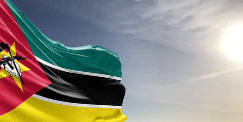 Mozambique national flag cloth fabric waving on beautiful grey sky Background. - obrazy, fototapety, plakaty