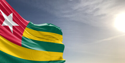 Togo national flag cloth fabric waving on beautiful grey sky Background.