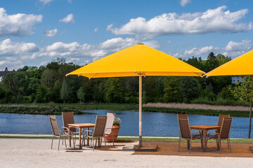 Gastronomie mit Sonnenschirm, Tisch Stühlen an einem See mit blauen Wolken