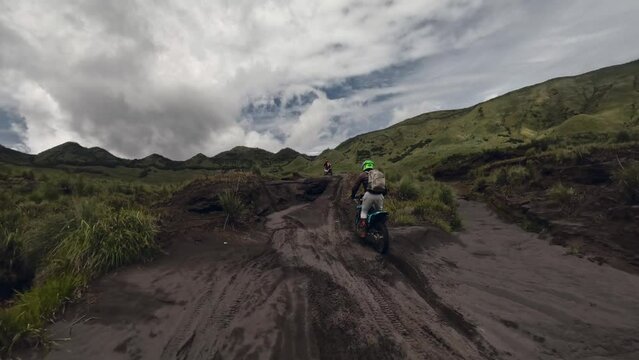 Group of active moto enduro bikers speed extreme riding between volcano at hilly terrain aerial view. FPV drone shot motorbike sport adventure motocross trip motorcycle transport cloudy sky mountain