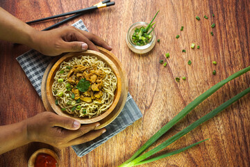 Noodles with Chicken, in Indonesia it is known as Mie Ayam. Served with green vegetable chili sauce in a bowl on wooden background by hand