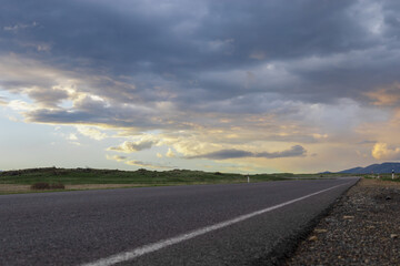 Fototapeta premium Scenic perspective of an empty highway against a vibrant backdrop of dramatic, colorful clouds during the golden hour