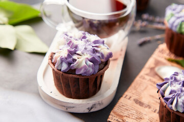 Purple aesthetics trendy floral cupcake and cup of coffee close up. Violet french no sugar dessert with lilac flowers
