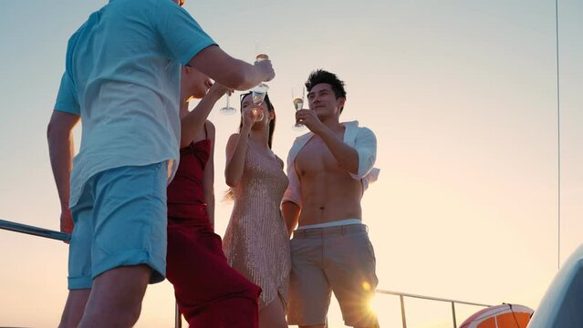 Group of young diverse people drinking wine and champagne while having sail boat party. Group of men and women friends enjoy party and having fun together while yacht sailing at sunset