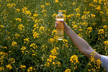 A man's hand holds a bottle of rapeseed oil