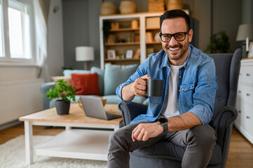 Portrait of confident male entrepreneur holding coffee cup and smiling cheerfully while sitting on...