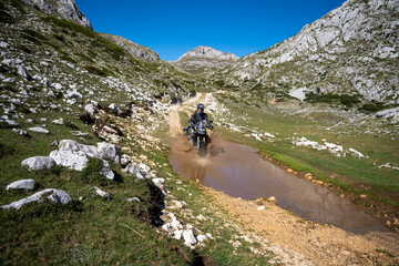 Young man wearing body armour riding through a deep puddle on the Trans Euro Trail in Montenegro