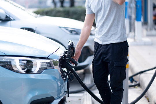 Close up of man hand holding green energy fluel dispenser infront of his electronic car, while standing and waiting, using Clean energy to decrease polution in the world comncept.