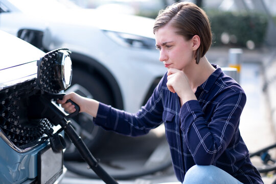 White Beautiful woman using fluel dispenser charging electrical car with serious emotion. USing green energy concept in travel on road trip.