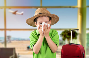 Child in hat blowing into wipe suffering from flu symptoms at airport.