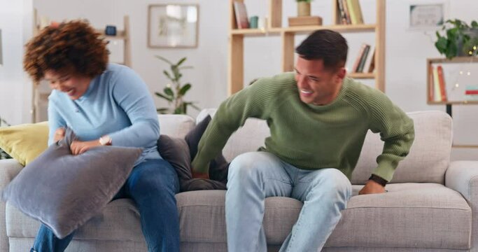 Pillow fight, happy couple and fun in living room for love, silly game and energy at home. Cushion, fighting and excited man being playful with young woman, partner and laughing together on couch