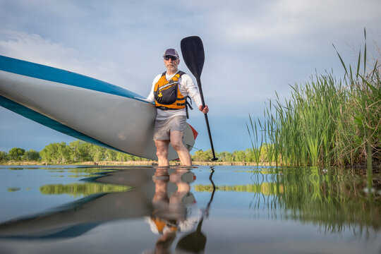 senior male paddler is launching a stand up paddleboard on a calm lake in spring, frog perspective from an action camera at water level