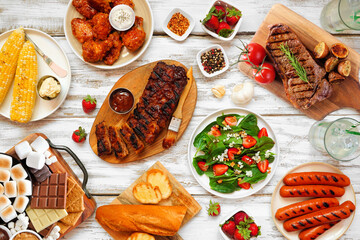 Summer BBQ food table scene over a white wood background. Variety of grilled meats, vegetable...
