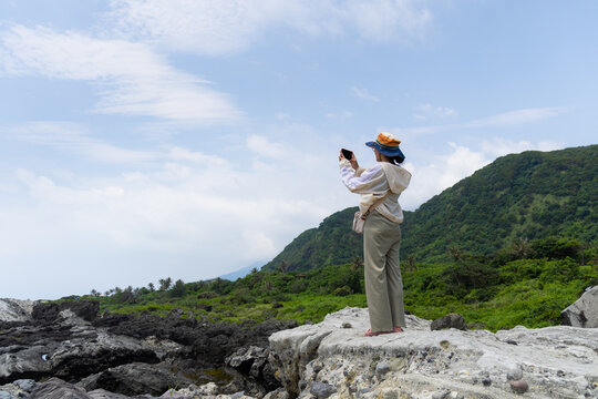 Hiking woman use cellphone to take photo and stand beside the beach