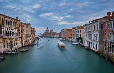 Fototapeta na wymiar Old canal with bridge, gondola, houses, flowers in cloudy weather. Venice