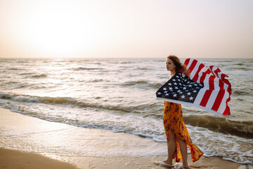 Young woman with american flag on the beach at sunset. 4th of July. Independence Day. Patriotic holiday.
