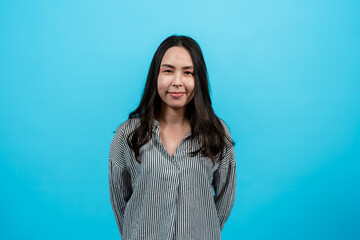 Obraz premium Portrait Asian woman in casual shirt with long sleeves looking straight ahead. Smile at the camera that is capturing it. Indoor studio isolated on blue background