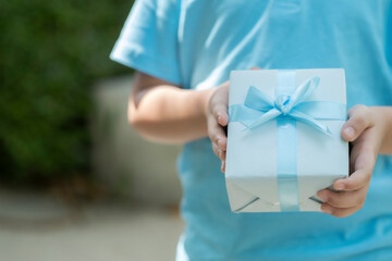 Blue paper wrap box gift with blue ribbon in little hand of child and space.