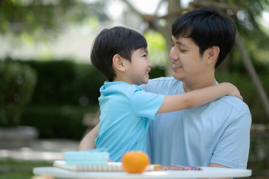 Father and son embrass and look each another with smile of love and happiness, Father's day concept, relationship with dad and child in family.