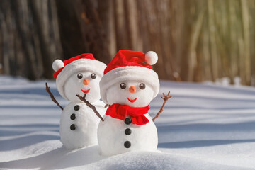 View of a couple of snowmen in a santa hats on their heads in a winter forest. Holiday christmas background with copy space for text