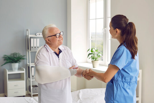 Happy, grateful male patient exchanging handshakes with doctor. Senior man with broken arm shaking hands with young female surgeon, thanking her for help and smiling. Injury treatment concept