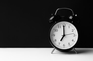 Black alarm clock on white table on black background.