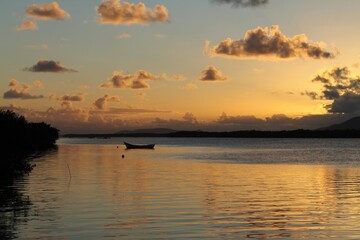 Silhouette of a small traditional Brazilian fishing canoe in the calm waters of a river, reflecting the yellow and orange colors of the sunset on Cardoso Island in Cananeia - SP