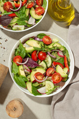 Fresh green salad with tomatoes, cucumbers, radish, sweet pepper and avocado in a white plate on a gray background.