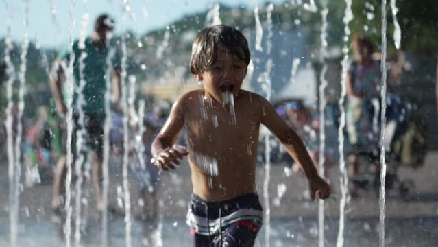 One happy small boy running toward water jets at outdoor park during summer vacations