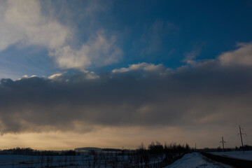 Winter sunset landscape, snow-covered field and in the distance there are CHP chimneys on the horizon and smoke comes out of them