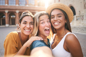 Three cheerful girls friends in summer clothes taking a selfie outdoors at the touristic urban...