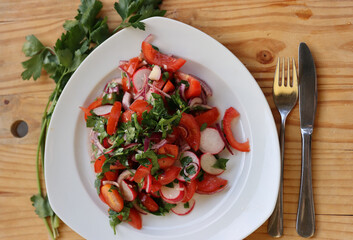 Fresh vegetables salad served on the white plate on the vintage cracked wooden cutting board. Organic tomatoes, parsley, celery, reddish with olive oil. Table setting. Top view.