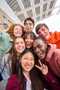Vertical multi-ethnic group smiling student boys and girls taking selfie outdoors. Happy lifestyle concept of friendship in multicultural young people having fun day together. Seven partners enjoying.