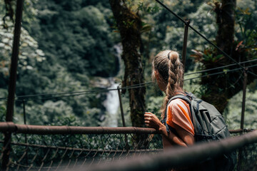 Rear view of blonde woman hiker crossing suspension bridge inside rain forest