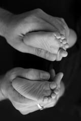 Black and white shade beautiful shape hands of mother, hold tiny newborn baby feet on black background with love, care, family safety and protection, child with premature birth concept or NICU care