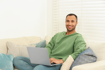 Smiling African American man with laptop on sofa in room