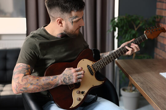 Handsome hipster man playing guitar in stylish room