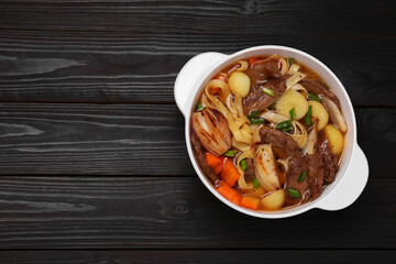 Pot of delicious vegetable soup with meat, noodles and ingredients on black wooden table, top view. Space for text