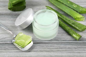 Obraz na płótnie Canvas Jar with natural gel, spoon of peeled aloe vera and green leaves on light grey wooden table